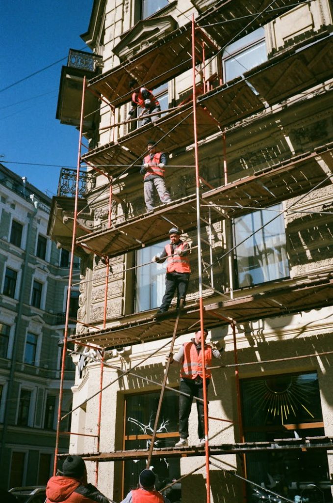 Services Construction workers on scaffolding renovating a building facade on a sunny day.